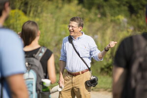 A man standing front of a crowd of out of focus students pointing.