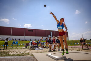 A woman throwing a shotput as other people watch from behind.