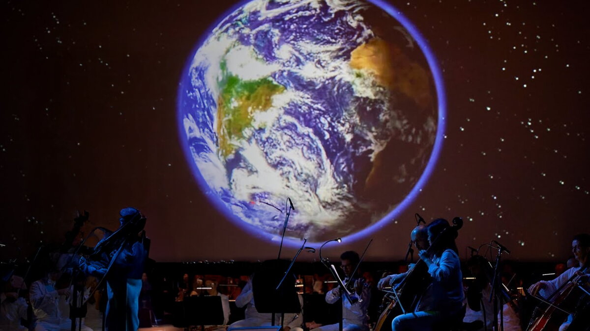 A symphony performing in front of a projection of the earth.