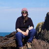Sarah Austin. A woman sitting on rocks by the sea.