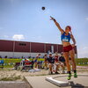 A woman throwing a shotput as other people watch from behind.