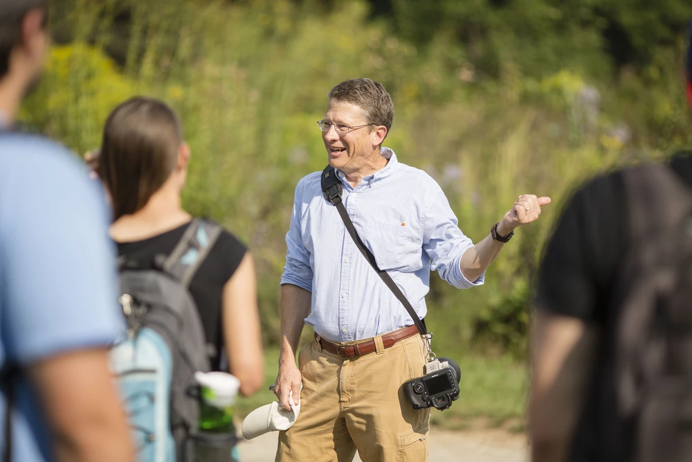 A man standing front of a crowd of out of focus students pointing.