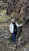 A person standing next to a rocky cliff dressed in winter clothing.